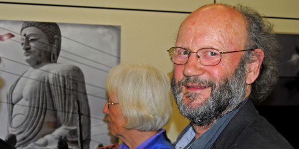 Künstler Horst Esser steht seitlich zur Kamera vor seiner Fotografie "building gods" und lächelt. Neben ihm steht eine Frau mit weißen Haaren