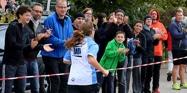 Eine Mitarbeiterin der Akademie für Politische Bildung läuft den Landkreislauf 2015. Am Straßenrand stehen Kollegen und andere Personen hinter Absperrband und feuern sie an