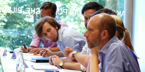 Sechs Teilnehmer der Planspiel-Werkstatt "Entwicklung von Politiksimulationen" sitzen nebeneinander an Tischen