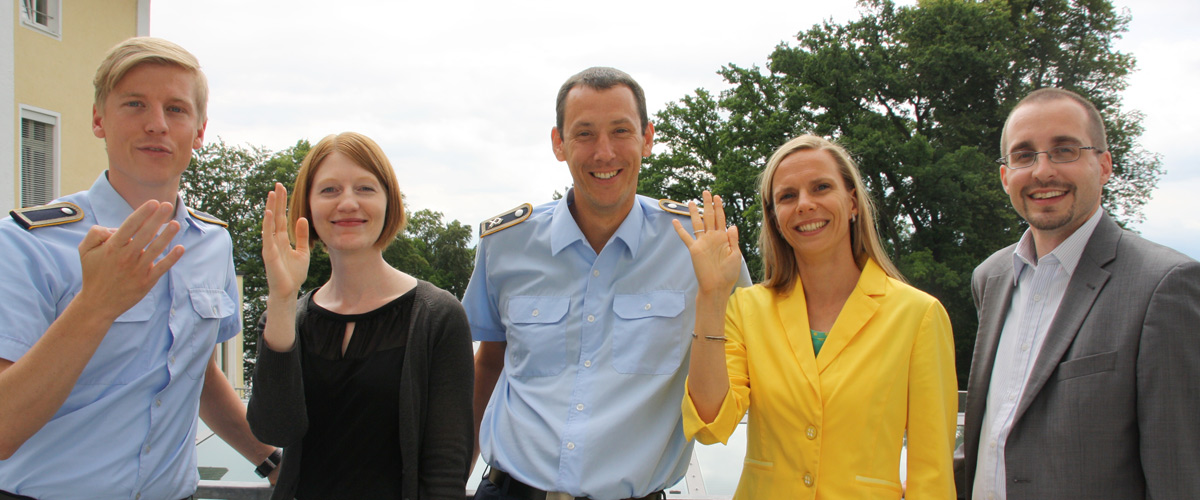Dorthe Siegmund, Arnold Kammel, Anja Opitz, Jochen Fröschle und ein weiterer Offizier der Bundeswehr stehen im Garten der Akademie für Politische Bildung und winken und lächeln in die Kamera