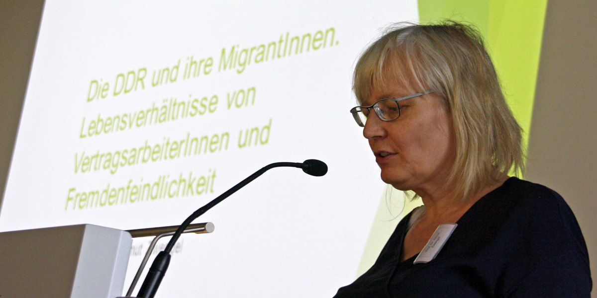 Almut Zwengel steht an einem Rednerpult in der Akademie für Politische Bildung und spricht. Links neben ihr ist eine Leinwand, auf der eine PowerPoint-Präsentation zu sehen ist