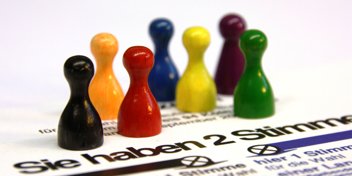 Sieben bunte Spielfiguren stehen auf einem Wahlzettel