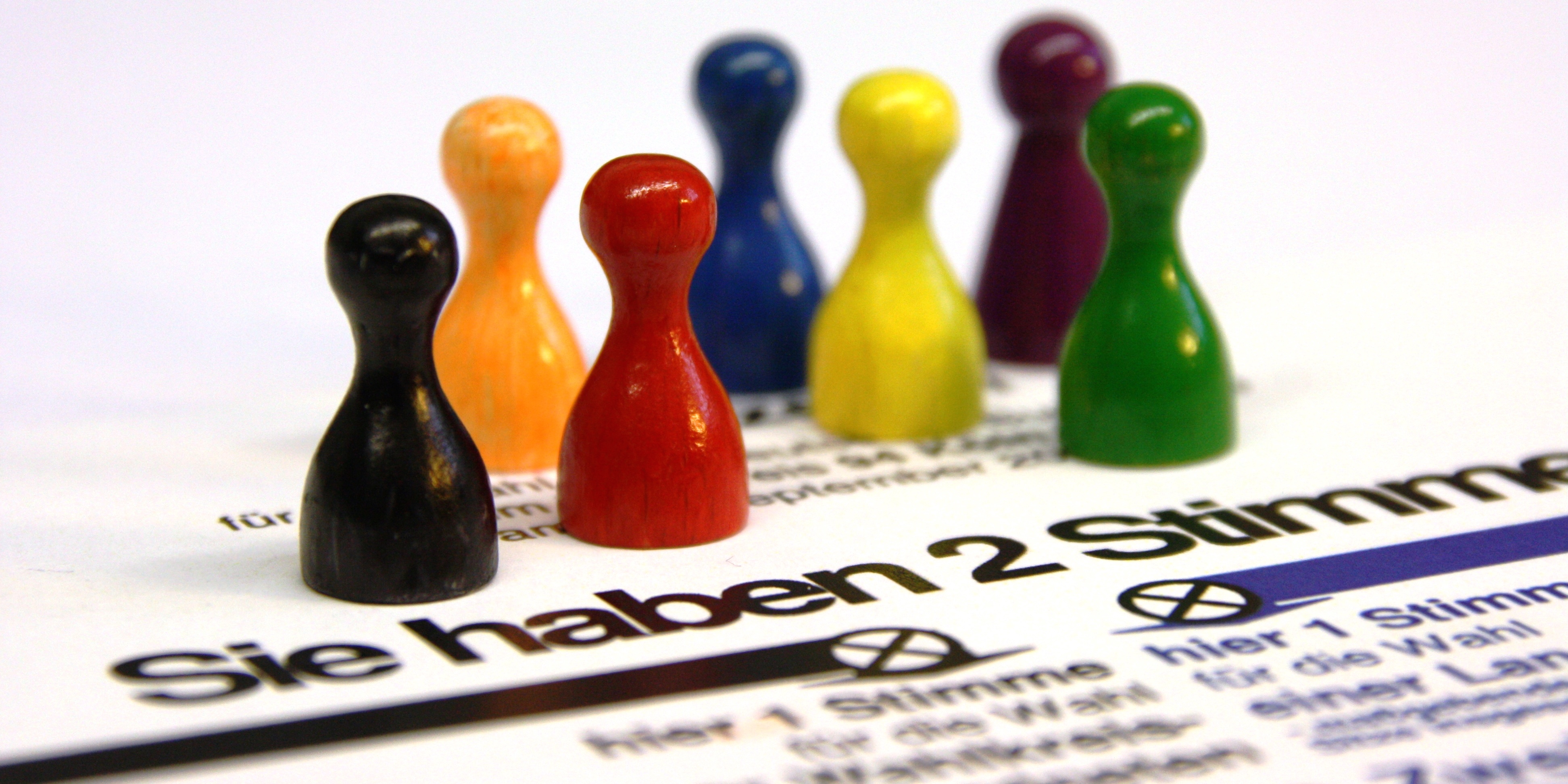 Sieben bunte Spielfiguren stehen auf einem Wahlzettel