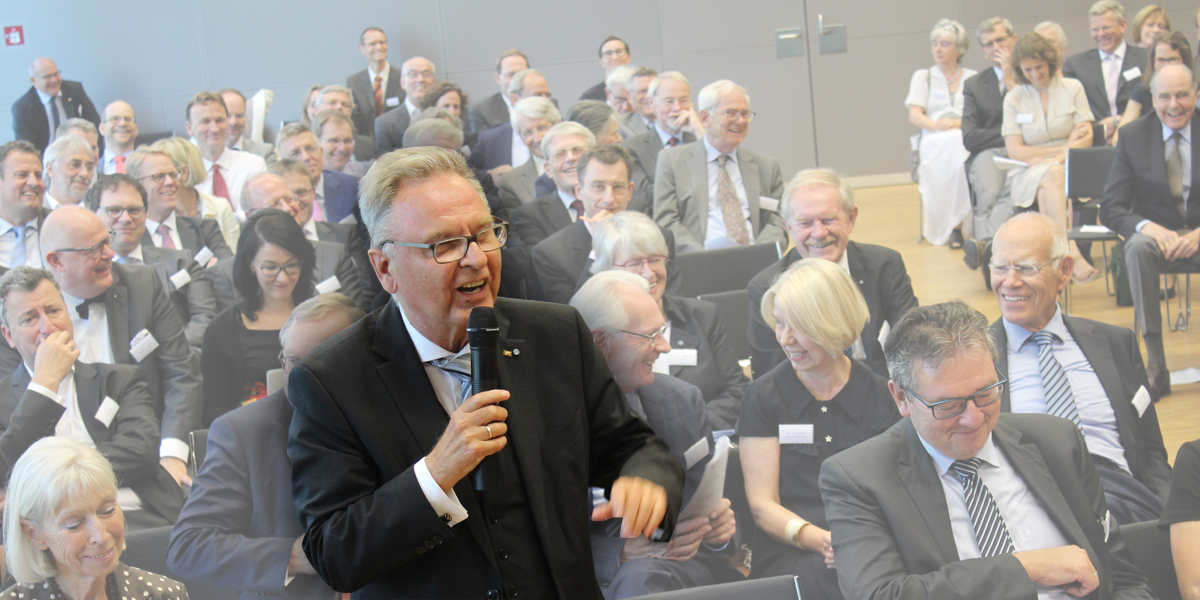 Im Hörsaal der Akademie für Politische Bildung sitzen die Gäste, die zum Symposium zur Verfassungspolitik zum 75. von Hans-Jürgen Papier gekommen sind und lachen. In der ersten Reihe steht Hans-Jürgen Papier, der ein Mikrofon in seiner linken Hand hält und ebenfalls lacht