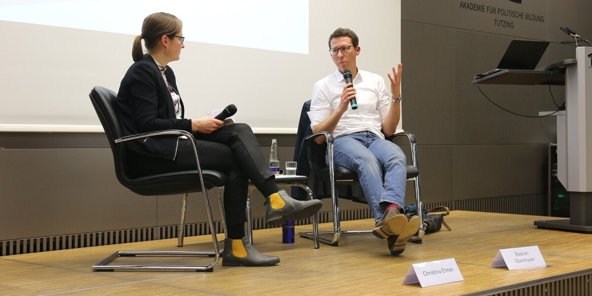 Christina Elmer und Bastian Obermayer sitzen auf dem Podium im Hörsaal der Akademie für politische Bildung. Beide halten ein Mirkofon in der Hand und führen ein Gespräch