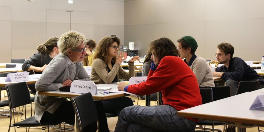 Mehrere Personen sitzen an verschiedenen Tischen im Hörsaal der Akademie für Politische Bildung Tutzing und unterhalten sich.