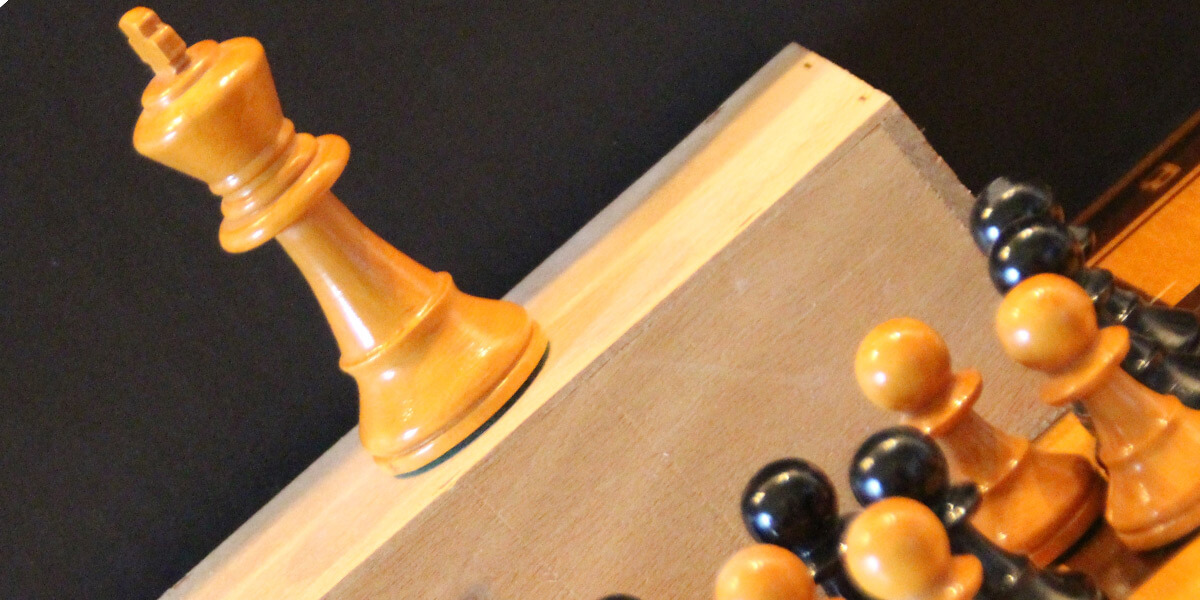 Nahaufnahme von Schachfiguren: Die Bauer stehen vor einem Holzklotz, auf dem der König steht.