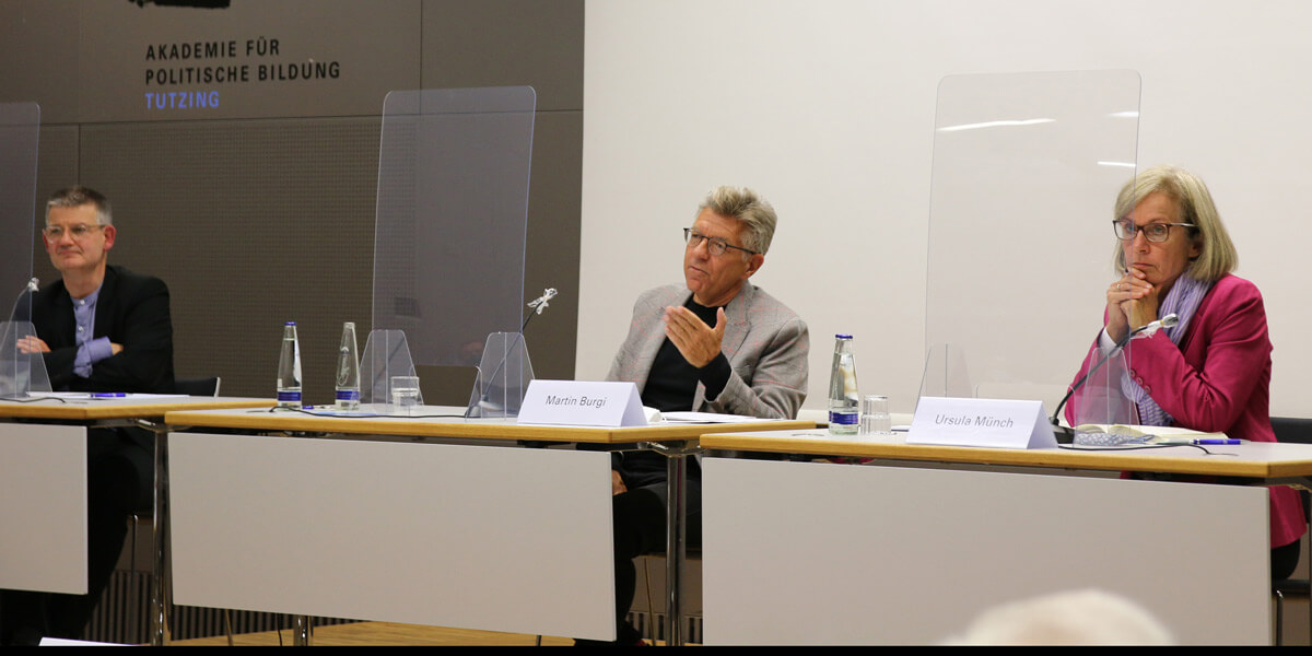 Johannes Wallacher, Martin Burgi und Ursula Münch sitzen jeweils an einem Tisch auf der Bühne des Hörsaals der Akademie für Politische Bildung Tutzing.