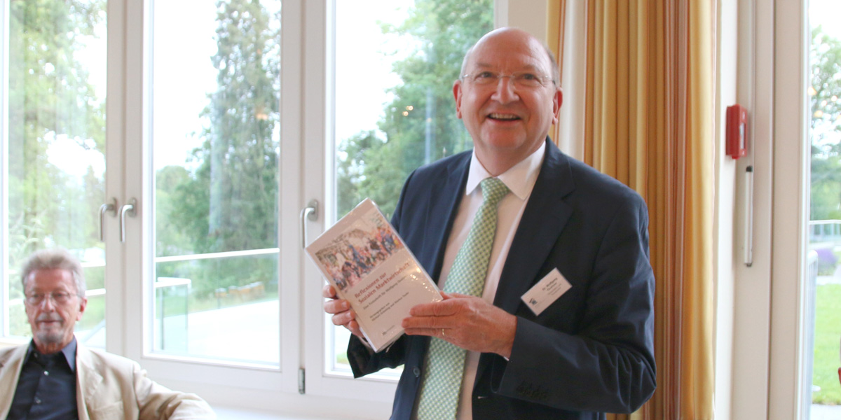 Wolfgang Quaisser hält ein Buch hoch und lächelt in die Kamera