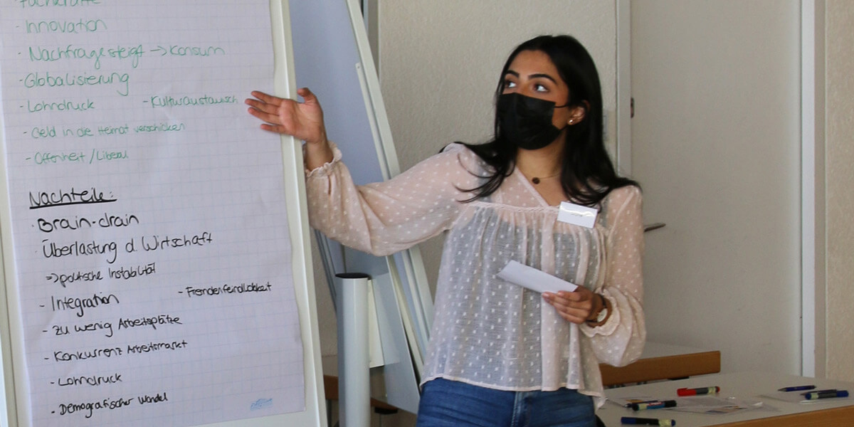 Eine Teilnehmerin der  Ideenwerkstatt "Zehn für Zukunft - Gesellschaftliche Veränderungen wahrnehmen und gestalten" steht rechts von einem Flipboard und erklärt etwas