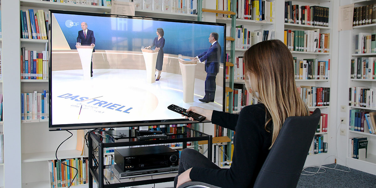 Frau sitzt vor dem Fernseher und schaut eines der Trielle von Annalena Baerbock, Armin Laschet und Olaf Scholz