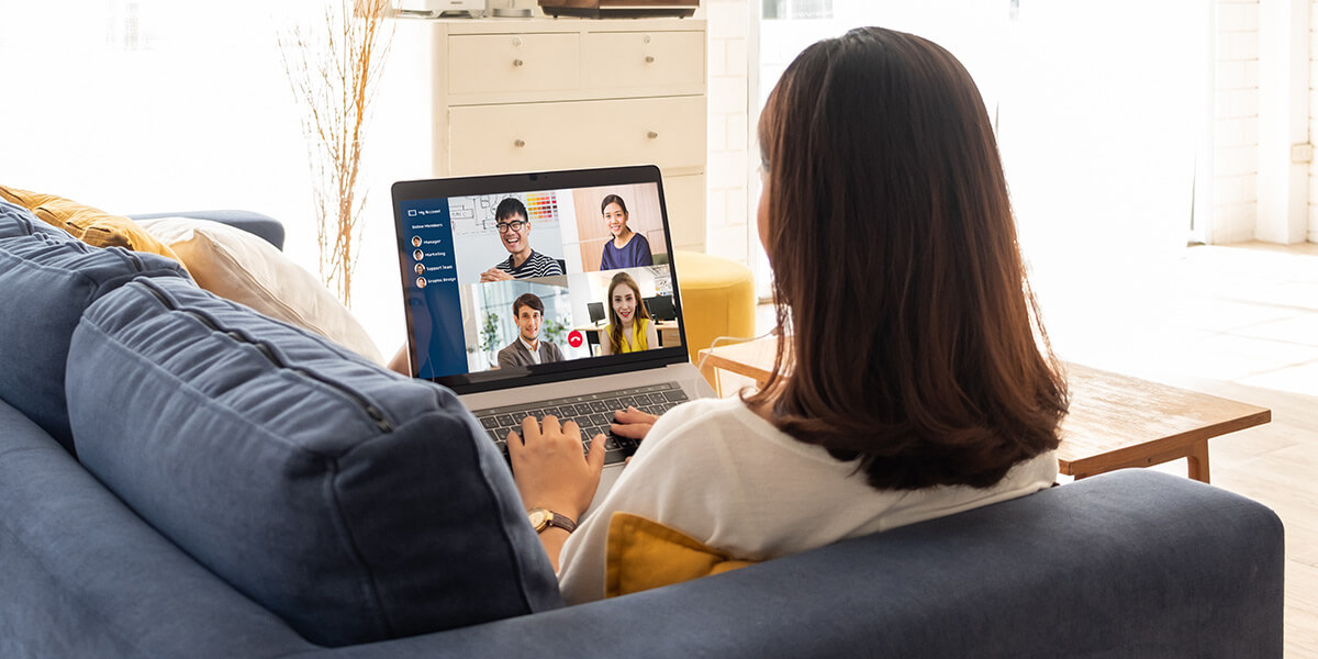 Frau sitzt mit Laptop auf der Couch und nimmt an einer Videokonferenz teil