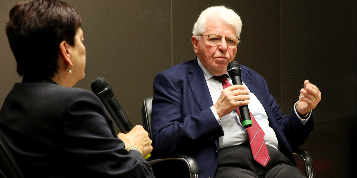 Rechts im Bild sitzt Heinrich Oberreuter und spricht in ein Handmikrofon. Links ist seine Gesprächspartnerin Daniela Philippi von hinten zu sehen.