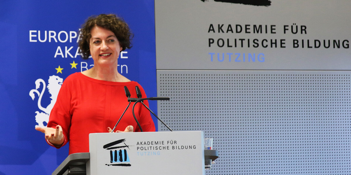 Karin Stögner spricht auf dem Podium der Akademie für Politische Bildung. Sie steht an einem Pult, und macht eine ausladende Geste mit dem rechten Arm. Hinter ihr ist ein Aufsteller der Europäischen Akademie Bayern zu sehen.