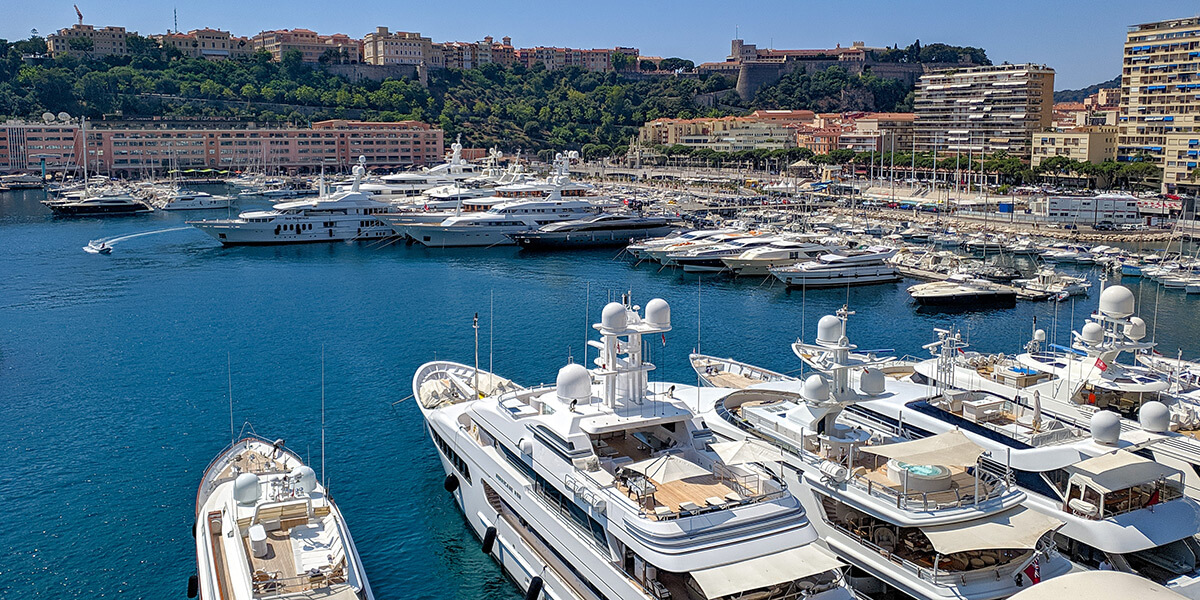 Der Hafen von Monaco: Im Vordergrund stehen Yachten in einem Halbkreis, im Hintergrund erheben sich die Gebäude der Stadt auf einem Hügel