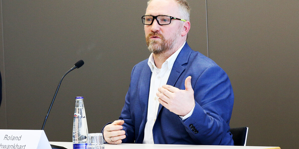 Roland Schwankhart sitzt auf dem Podium der Akademie für Politische Bildung und spricht.