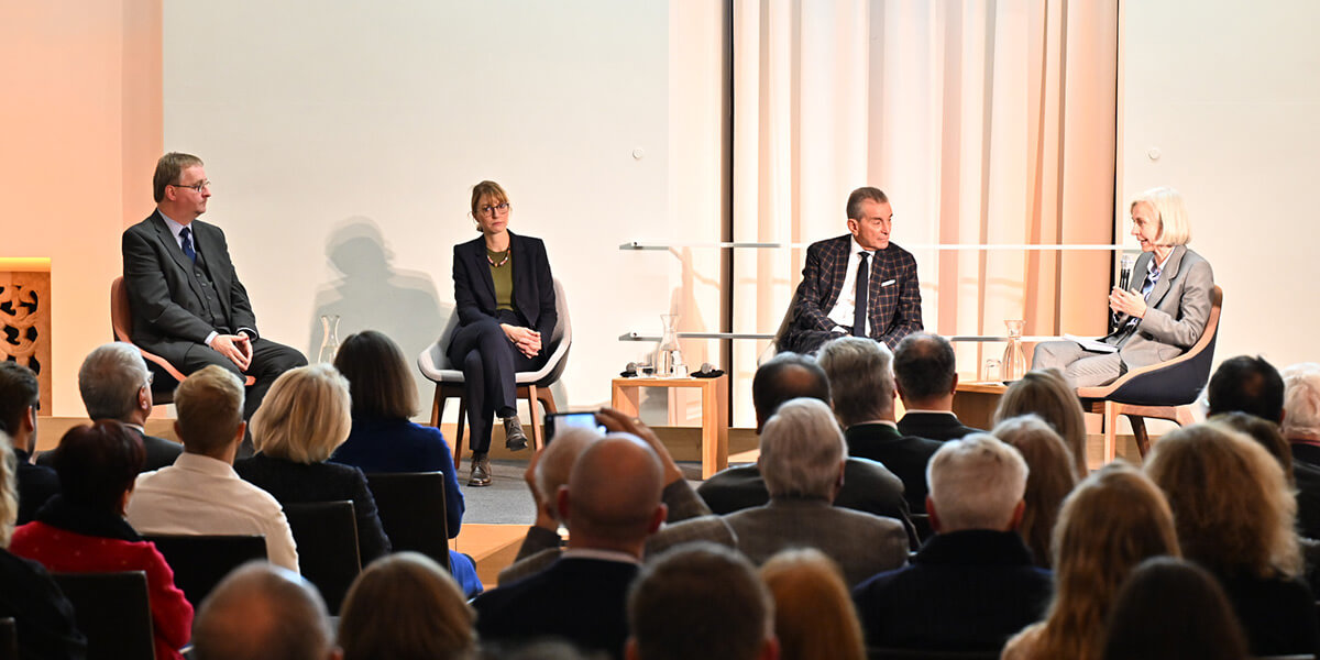 Ursula Münch sitzt im Senatssaal des Bayerischen Landtags auf dem Podium und spricht in ein Handmikrofon. Thomas Peterse, Astrid Séville und Michel Friedman sitzen links von ihr und wenden sich ihr zu. Im Vordergrund sind die Hinterköpfe des Publikums zu sehen.