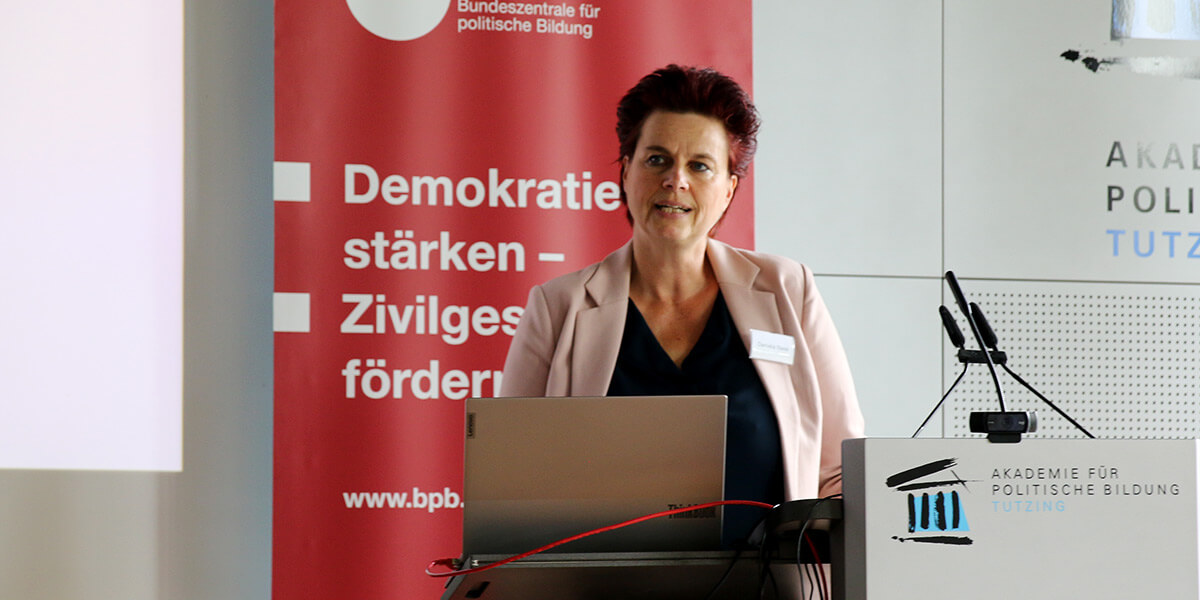 Daniela Nase steht am Pult der Akademie für Politische Bildung vor einem roten Aufsteller der bpb und spricht in ein Mikrofon.