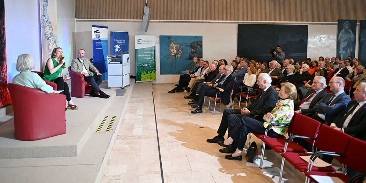 Terry Reintke sitzt auf dem Podium der Katholischen Akademie in Bayern und spricht in ein Mikrofon. Rechts von ihr sitzt Manfred Weber und links Ursula Münch. Beide wenden sich ihr zu. Rechts im Bild ist das Publikum zu sehen.
