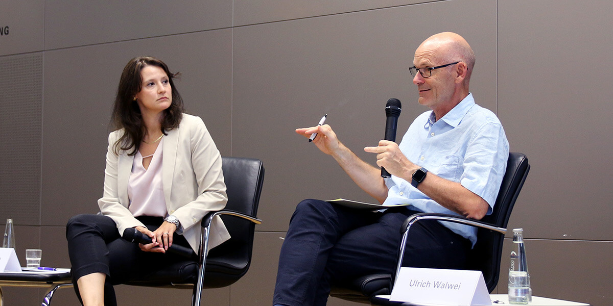 Ulrich Walwei sitzt auf dem Podium der Akademie für Politische Bildung und spricht in ein Mikrophon. Links von ihm sitzt Giulia Mennillo und schaut ihn an.