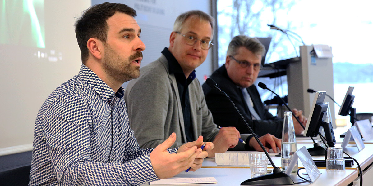 Pablo Jost sitzt auf dem Podium der Akademie für Politische Bildung und spricht in ein Mikrofon. Rechts von ihm sitzen Gero Kellermann und Winfried Bausback und wenden sich ihm zu.