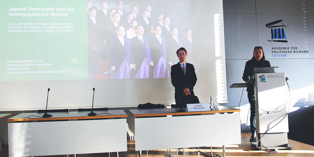 Saskia Hieber spricht am Pult. Yosuke Buchmeier steht daneben. 