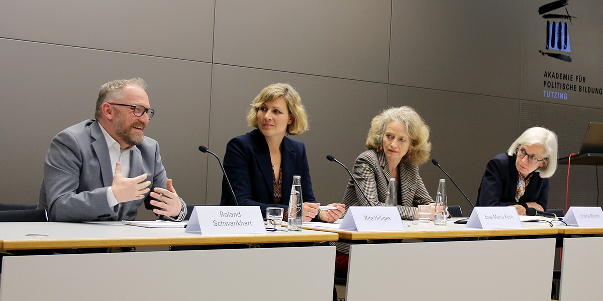 Roland Schwankhart sitzt auf dem Podium der Akademie für Politische Bildung und spricht in ein Mikrofon. Rechts neben ihm sitzen Rita Hilliges, Eva-Maria Kern und Ursula Münch und wenden sich ihm zu. 