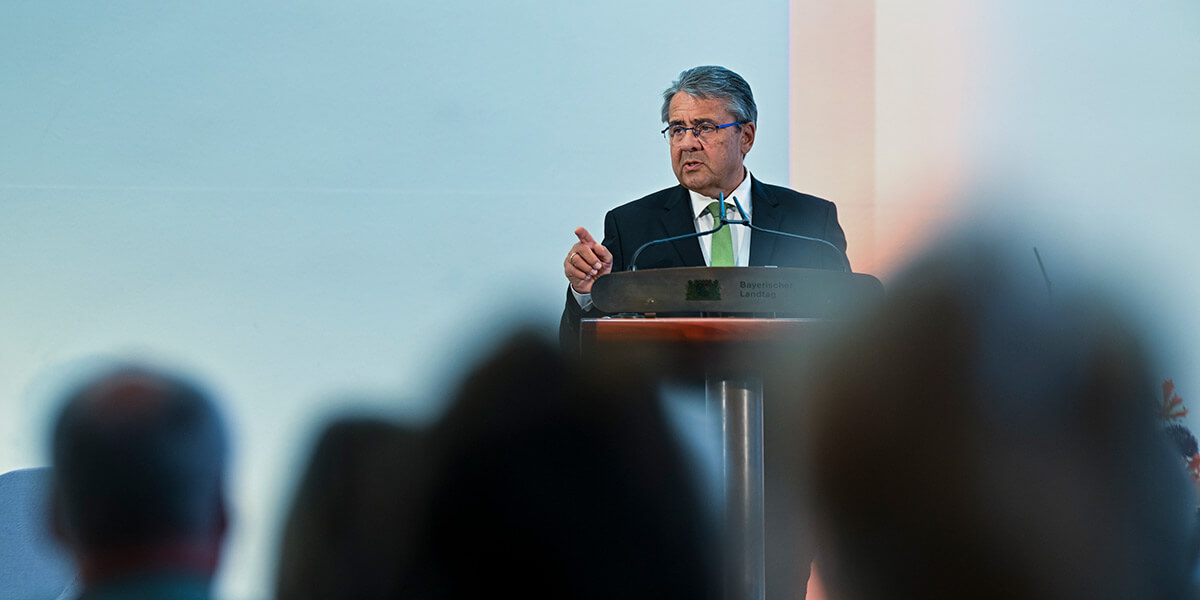 Sigmar Gabriel steht an einem Pult des Bayerischen Landtags, gestikuliert und spricht. Im Vordergrund sind verschwommen die Hinterköpfe des Publikums zu sehen.