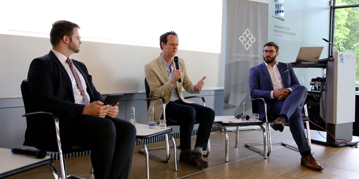 Wolfgang Mühlberger sitzt auf dem Podium der Akademie für Politische Bildung und spricht in ein Mikrofon. Links neben ihm sitzt Christian Rucker, rechts neben ihm sitzt Stefan Lukas und beide wenden sich ihm zu.