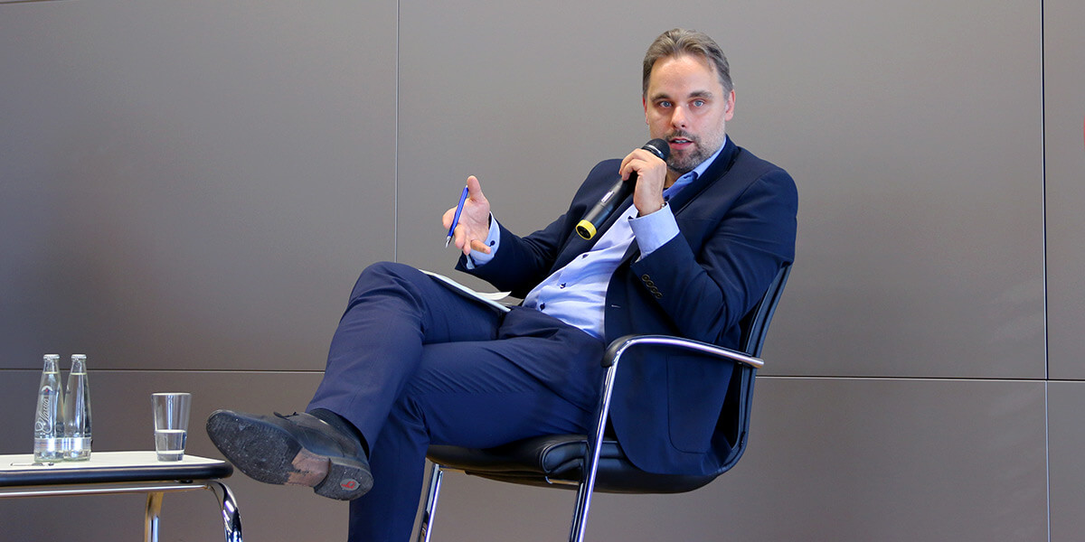 Rudolf Kučera sitzt auf dem Podium der Akademie für Politische Bildung und spricht in ein Mikrofon.