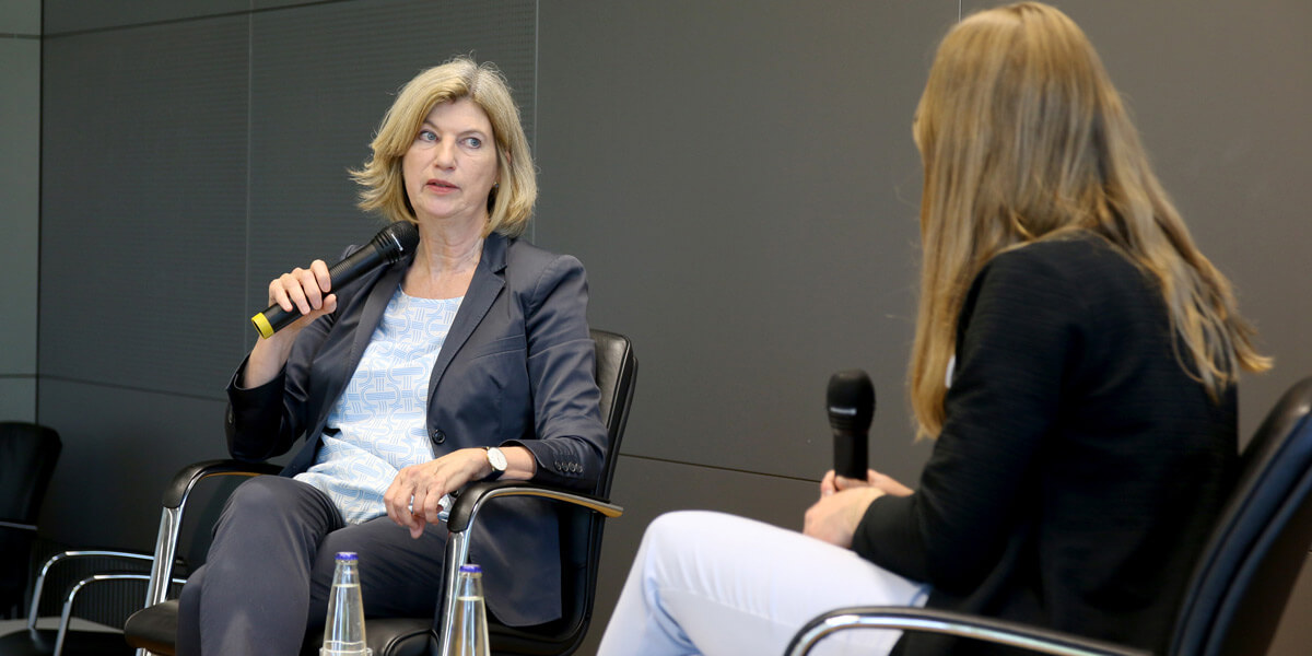 Marie-Janine Calic sitzt auf dem Podium der Akademie für Politische Bildung und spricht mit einem Mikrofon zu Beate Winterer, die sich ihr zuwendet.