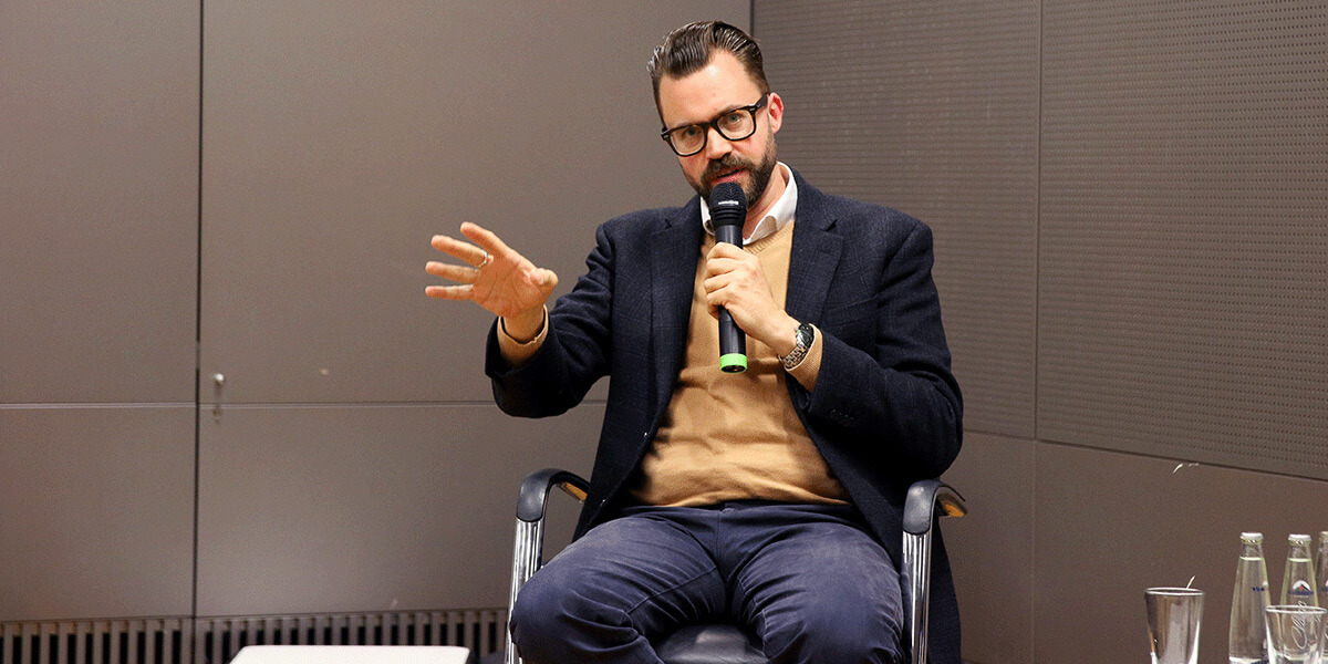 Marcel Lewandowsky sitzt auf einem Stuhl und spricht in ein Mikrofon.