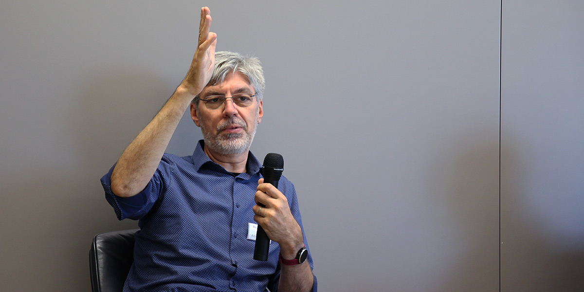 Alin Albu-Schäffer sitzt auf dem Podium der Akademie für Politische Bildung und spricht in ein Mikrofon. Er hebt dabei seine rechte Hand nach oben.