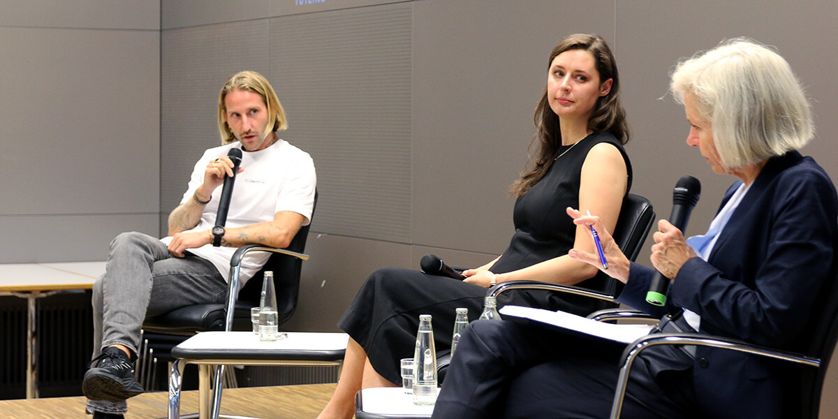 Simon Bölts sitzt auf dem Podium der Akademie für Politische Bildung und spricht in ein Mikrofon. Rechts von ihm sitzen Katharina Nocun und die Ursula Münch. Münch spricht ebenfalls in ein Mikrofon.