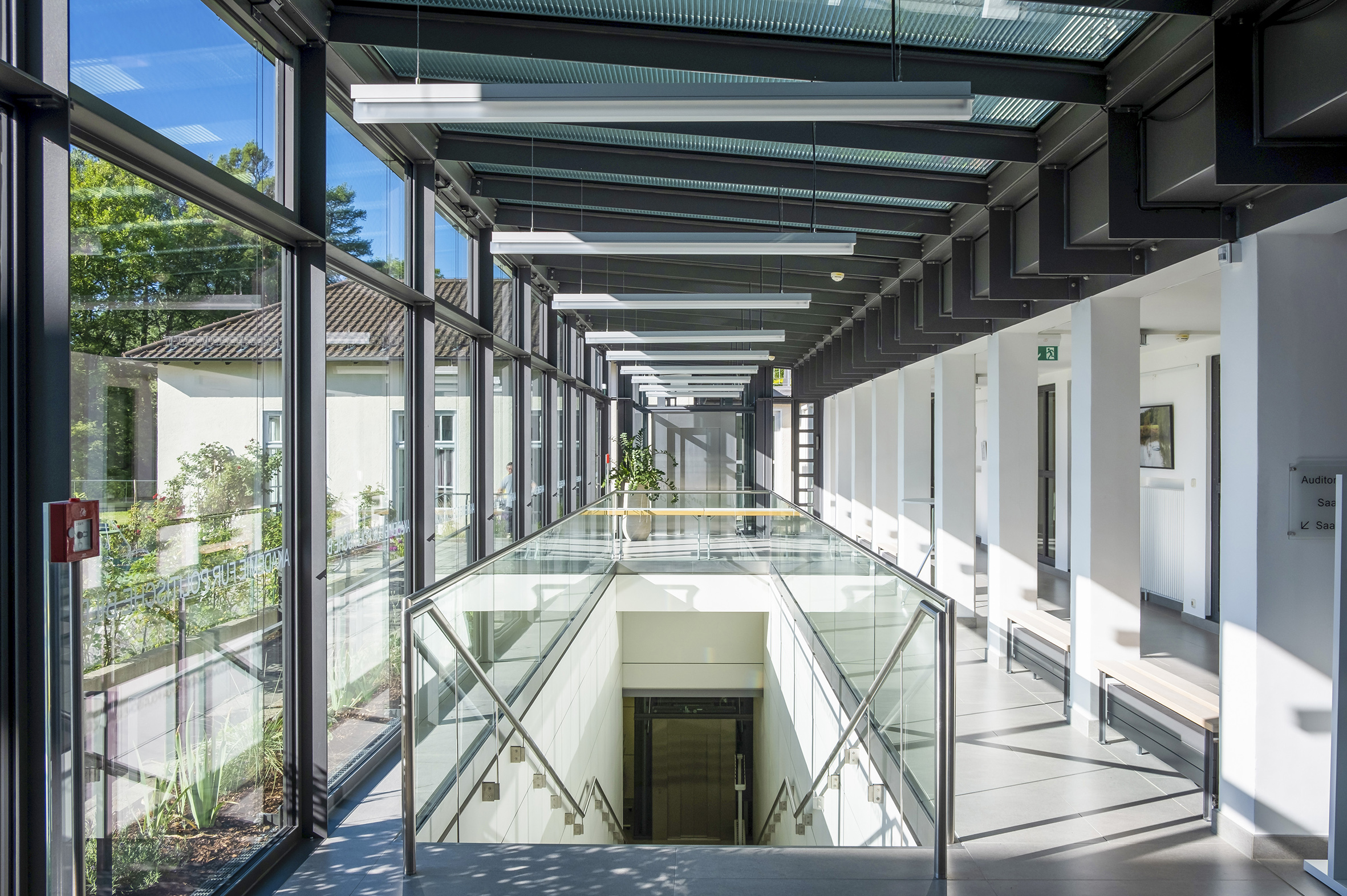 Im Vordergrund ist eine Treppe in einem verglasten Raum in der Akademie für Politische Bildung, im Hintergrund die Türen eines Aufzugs.