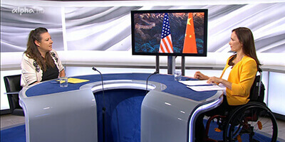 Links sitzt Saskia Hieber an einem großen runden Tisch im Studio von alpha-demokratie, rechts Mirjam Kottmann. Im Hintergrund ist ein Bildschirm zu sehen