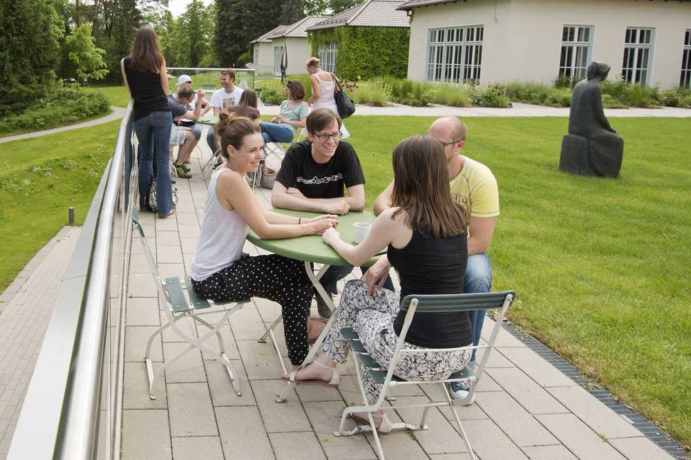 Junge Menschen sitzen um einen Tisch im Rosengarten der Akademie für Politische Bildung. Im Hintergrund ist eine weitere Menschengruppe.