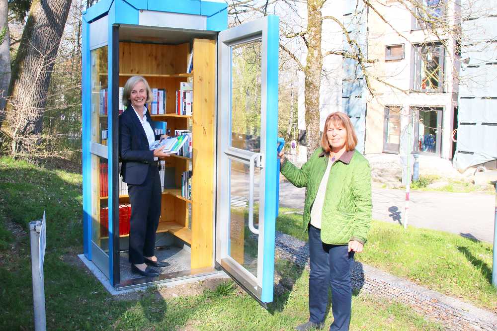 Ursula Münch steht mit einem Stapel Bücher in der Bücherzelle der Akademie für Politische Bildung, Renate Heinz hält die Tür auf.