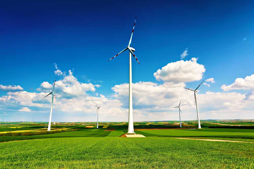 Mehrere Windräder stehen auf grünen Äckern. Im Hinergrund sind blauer Himmel und Wolken.