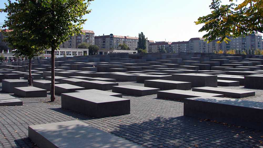 Denkmal für die Opfer des Holocaust in Berlin: Ein Meer aus Steinquadern, rechts und links jeweils ein Baum, im Hintergrund Wohnhäuser.